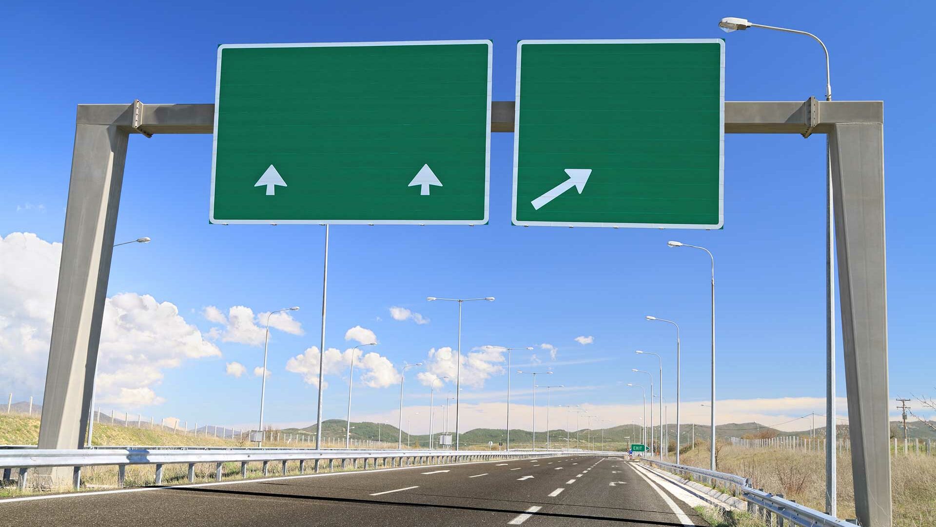 Overhead green highway signs showing two lanes continuing straight and one lane exiting to the right.