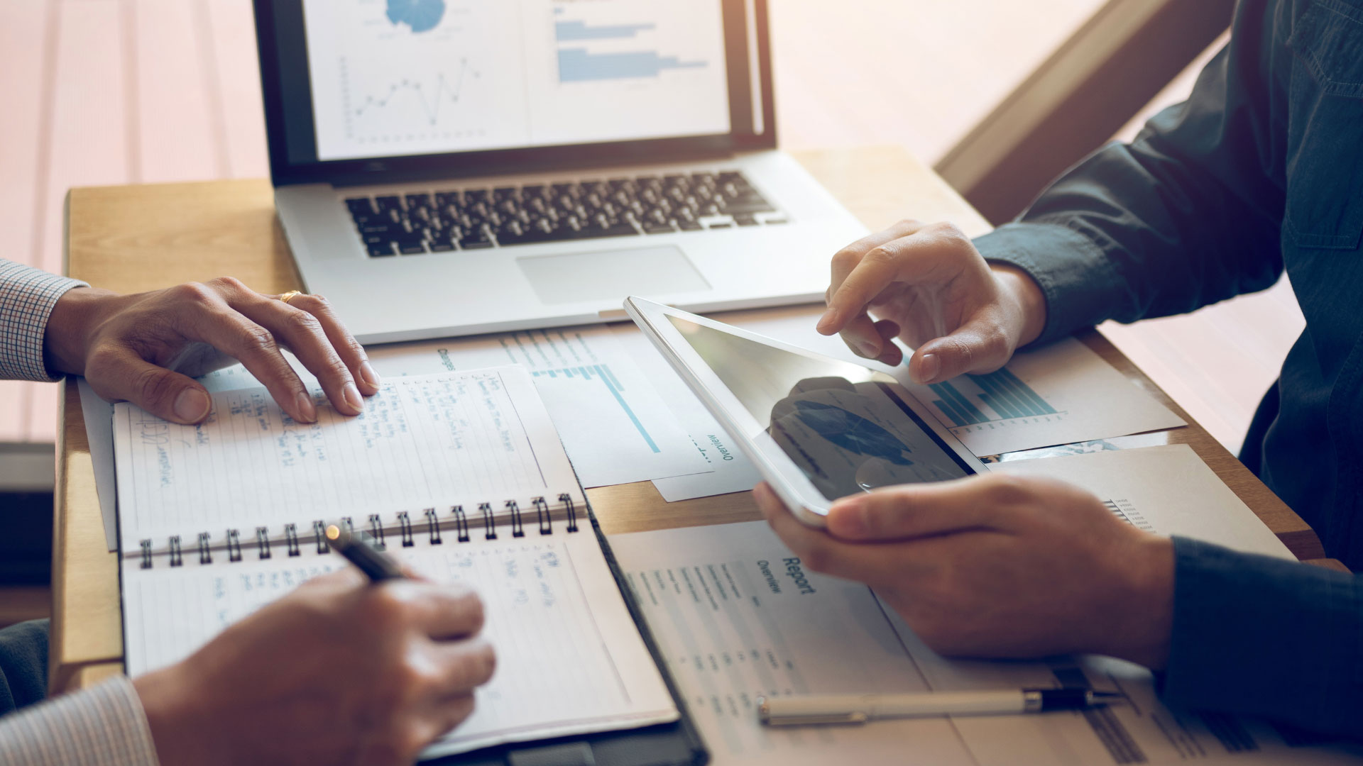 Two professionals analyzing reports on a tablet and printed documents.