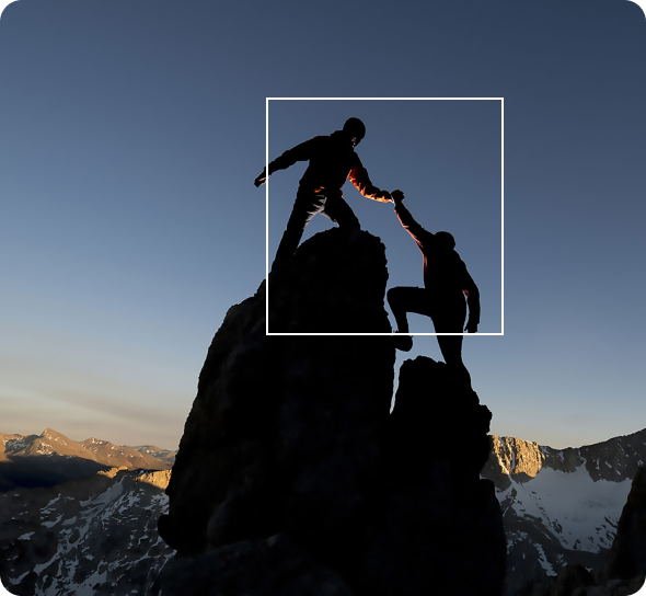 Two hikers helping each other reach a mountain summit