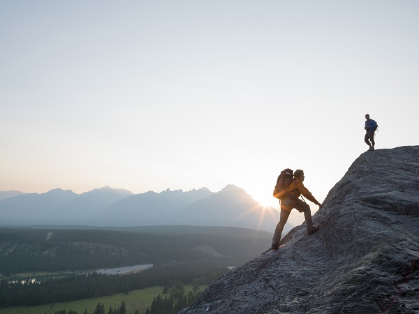 Two mountaineers clamber up a rock ridge at sunrise above a valley