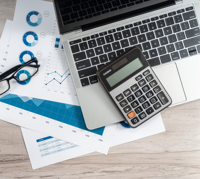 Office desk table with laptop, glasses and financial chart.
