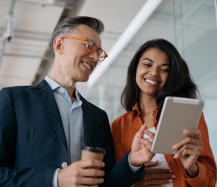 Two colleagues smiling while looking at a tablet.